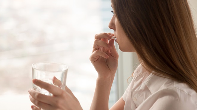 donna con bicchiere d'acqua in mano che prende un farmaco