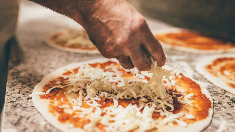mani mettono formaggio sulla pizza
