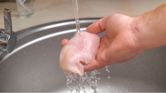 Mano di uomo lava pollo sotto rubinetto