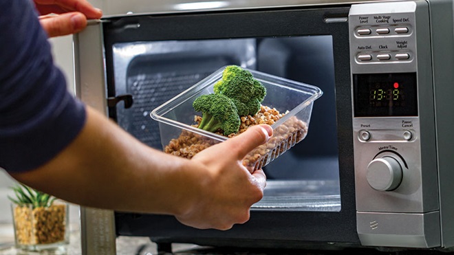 primo piano mano che mette contenitore con cibo nel microonde