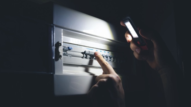 Quadro elettrico al buio e mano con torcia