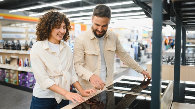 Coppia felice che sceglie un nuovo piano cottura a induzione, godendosi l'esperienza di acquisto in un moderno negozio di elettrodomestici.