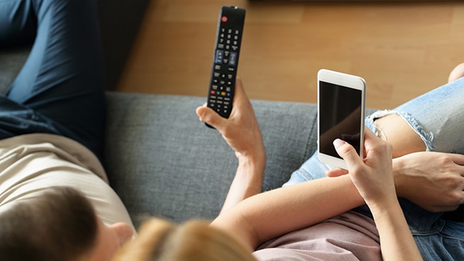 ragazzi sul divano con telecomando e smartphone in mano