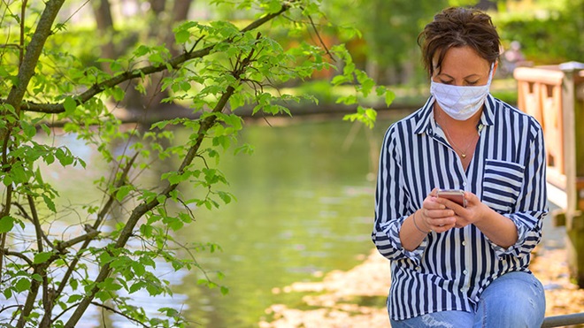 donna con nascherina che guarda smartphone