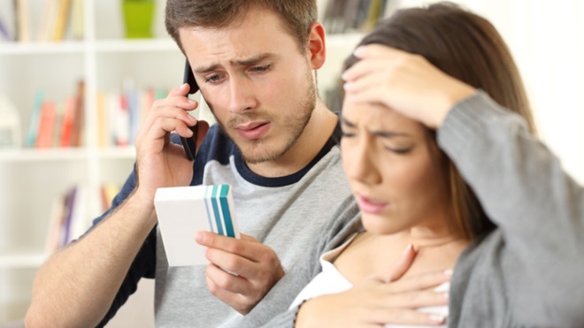 uomo al telefono guarda scatola farmaco con vicino donna che si porta la mano alla testa