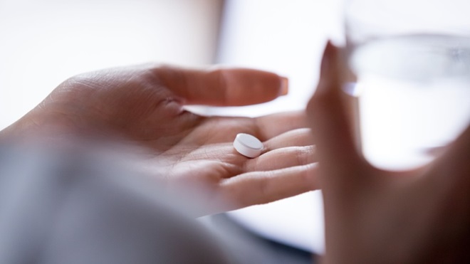 Pastiglia in mano a una donna con bicchiere
