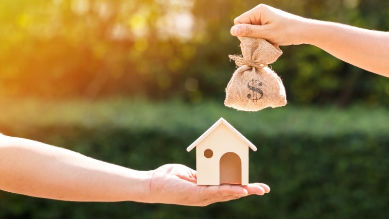 Mano con casetta e mano con sacchetto di dollari