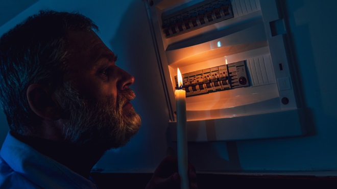 Uomo con candela accesa che esamina il quadro elettrico durante un blackout