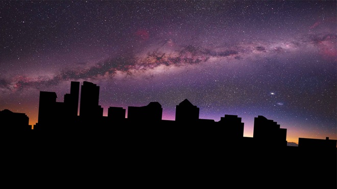 Skyline cittadino in silhouette al buio durante un blackout, sotto un cielo notturno stellato con la Via Lattea visibile