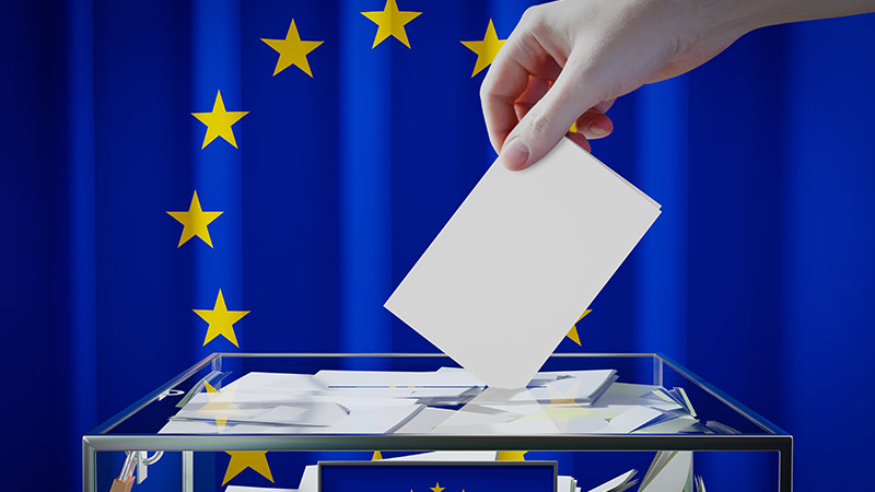 mano mette scheda nell'urna, sullo sfondo la bandiera europea