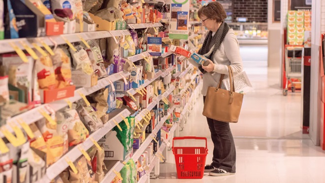 Signora di fronte agli scaffali del supermercato con in mano una confezione